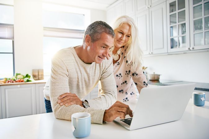 Older couple on a video call on their laptop in kitchen with tea