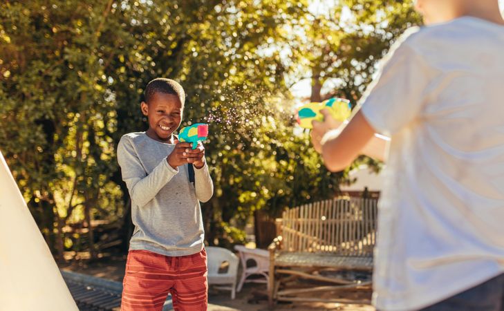 Two kids playing with water guns in backyard