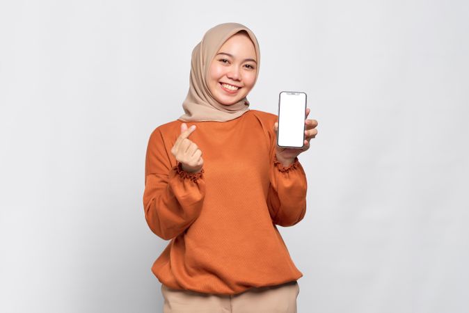 Muslim woman smiling at smart phone’s mock up screen making Korean heart gesture
