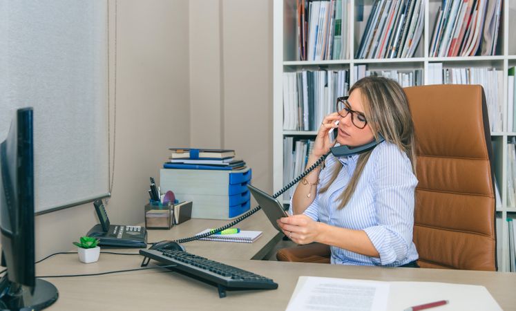 Busy businesswoman taking two calls phones in office