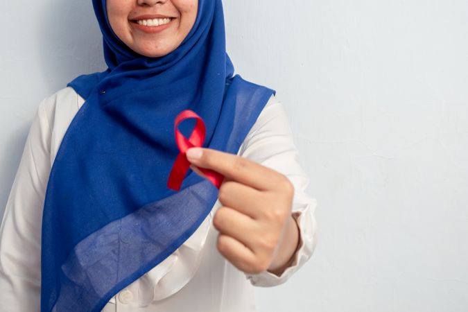 Happy Muslim Female Asian doctor or nurse holding Red ribbons, HIV awareness concept, world AIDS day, world cancer day with copy space
