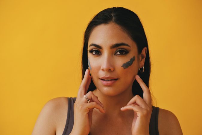 Happy Latina woman with her fingers to her face applying mud mask, copy space