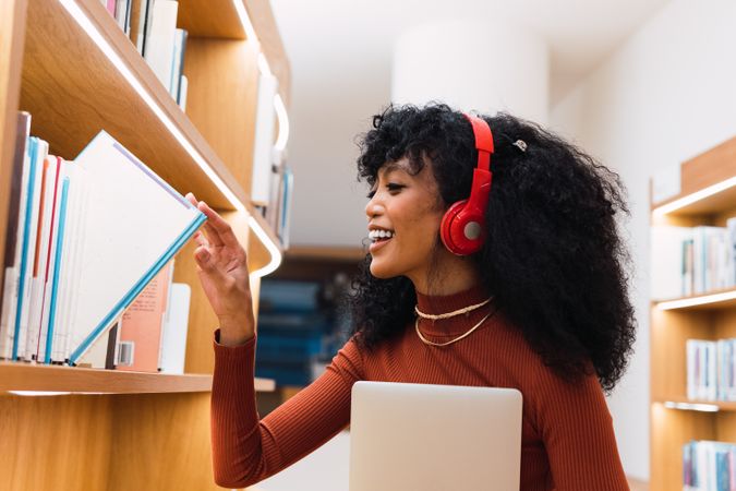 Satisfied woman with headphones taking book in library