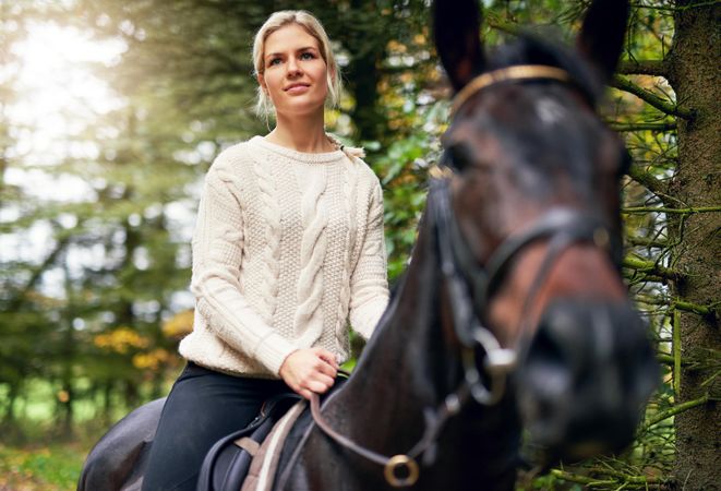 Beautiful woman sitting astride on her mare horse outdoors