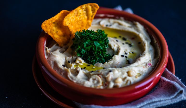 Close up of creamy hummus dip with olive oil, garnish and chips