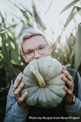 Blonde man with eyeglasses holding green pumpkin 489BKb