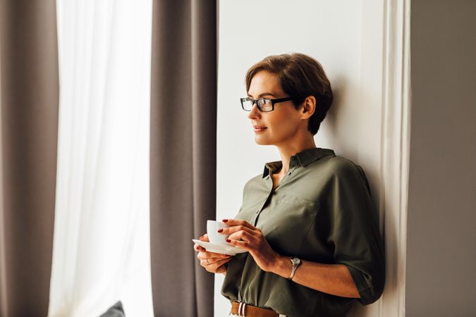 Woman leaning on wall  next to window with a cup and saucer