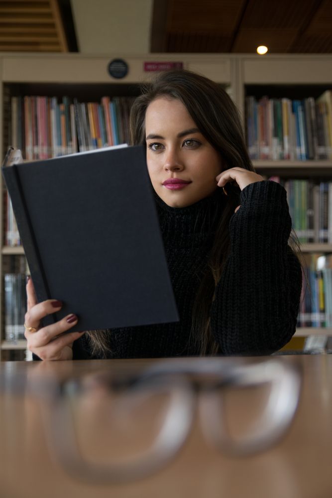 Woman sitting along bookshelves and holding open book