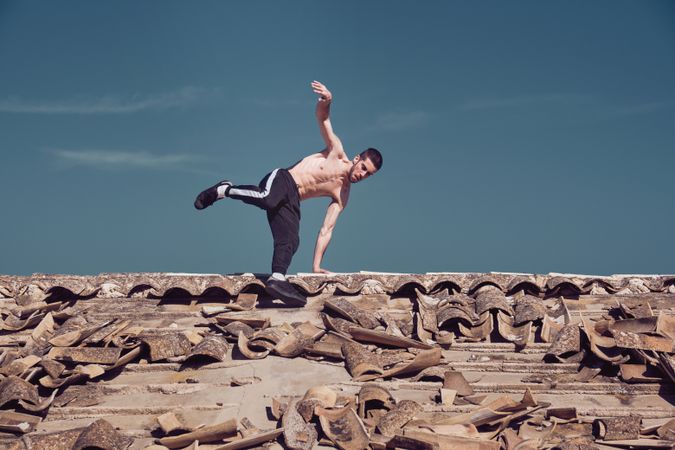 Athletic man performing handstand rotation while dancing breakdance on roof