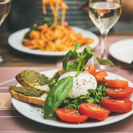 Man in striped shirt eating pasta with caprese salad in foreground, square crop