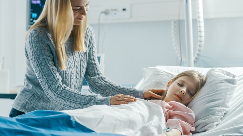 Cute Little Girl Sleeps on a Bed in the Children's Hospital, Caring Mother Covers Her with a Blanket and Caresses Her Forehead