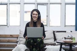 Beautiful Woman wearing headphones sitting on sofa and using laptop