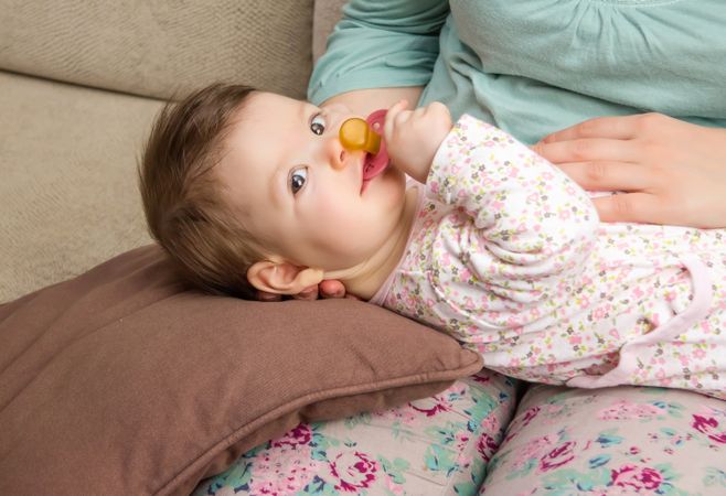 Cute baby lying on woman's lap with pacifier