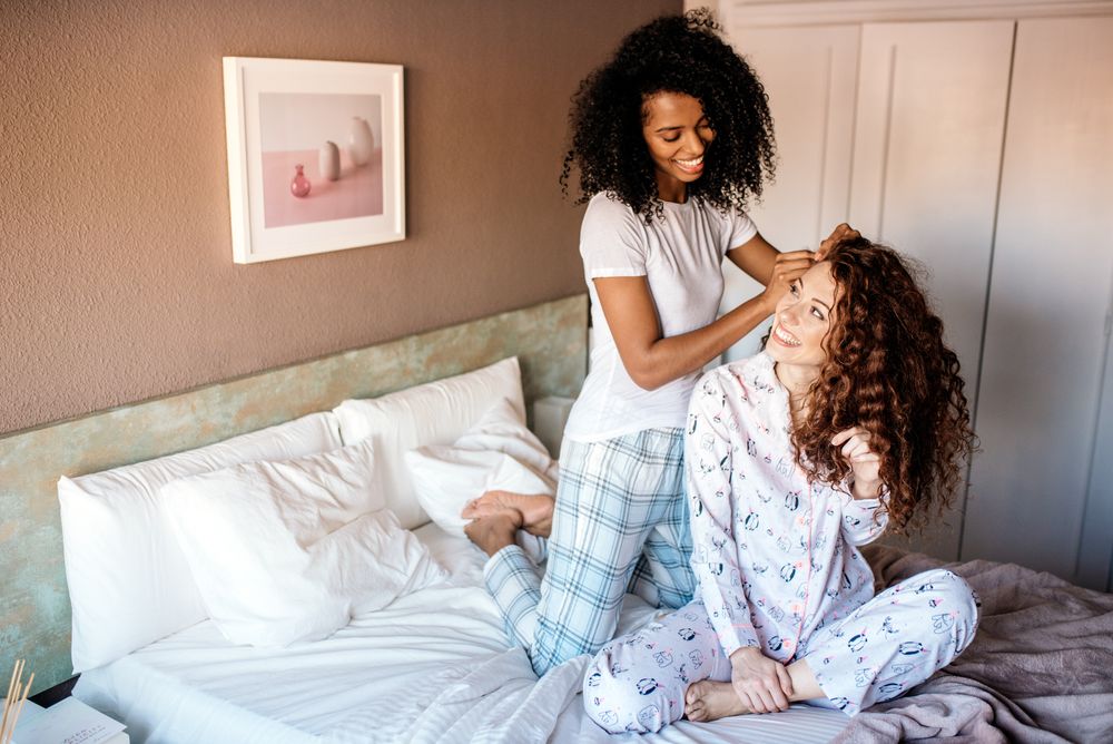 Woman combing another friend's hair in bed