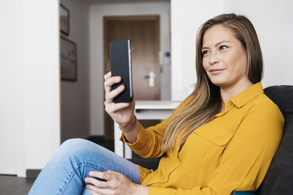 Beautiful adult female sitting on sofa while reading smartphone