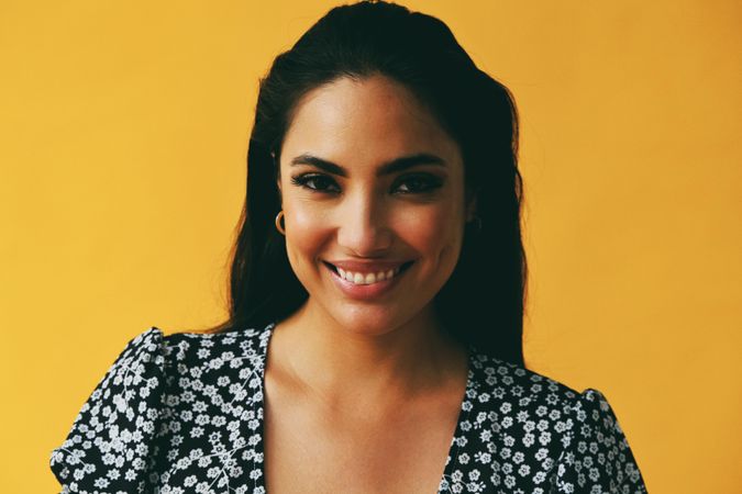Headshot of happy Hispanic woman looking away from camera in yellow room, copy space