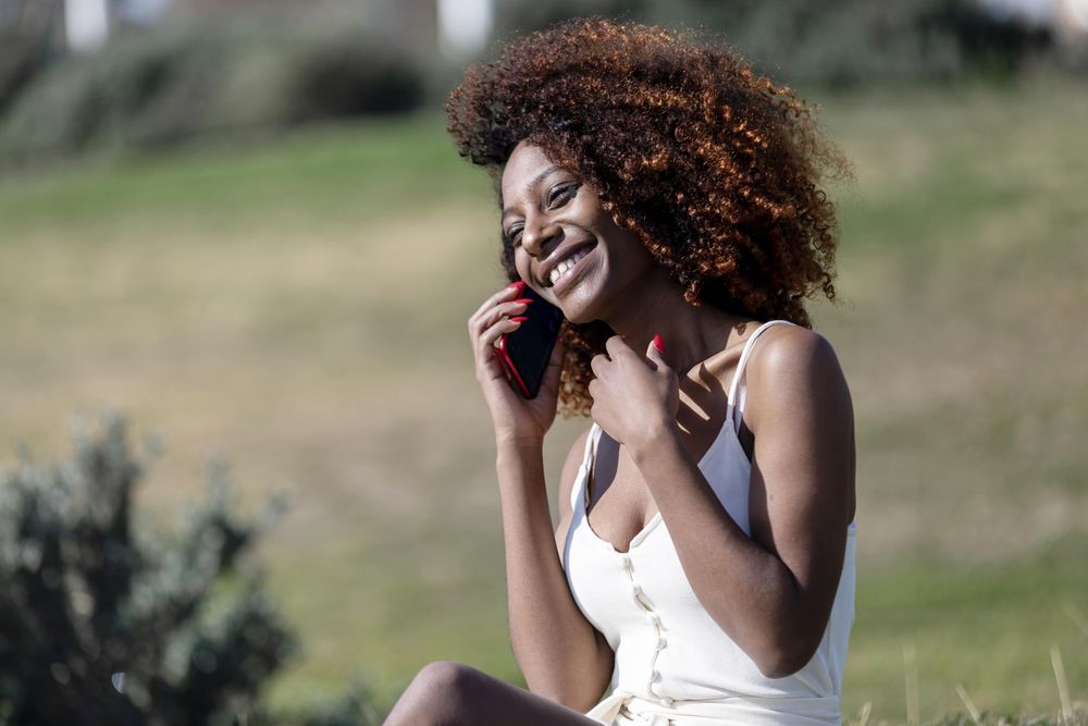 Female in light summer dress relaxing in park taking a phone call