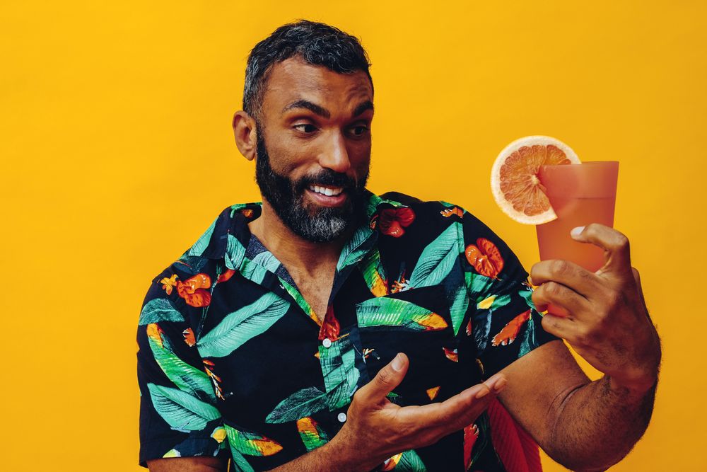 Black male sitting down amazed at his cocktail in yellow room, copy space
