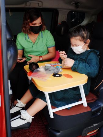 Mother and young daughter wearing facemasks sitting in a minivan