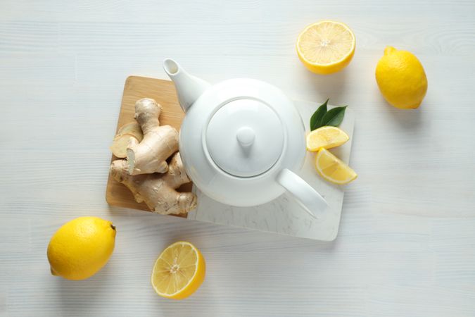Teapot with tea, lemon and ginger on board on light background, top view