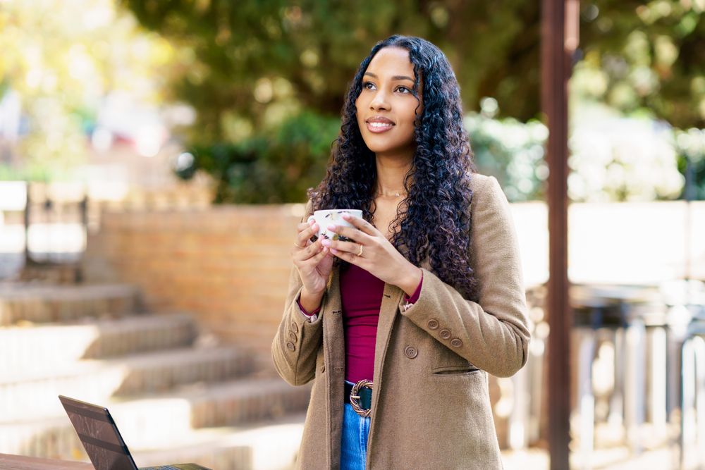 A Confident Woman Happily Enjoys A Cup Of Coffee While Outdoors In A Relaxing Setting