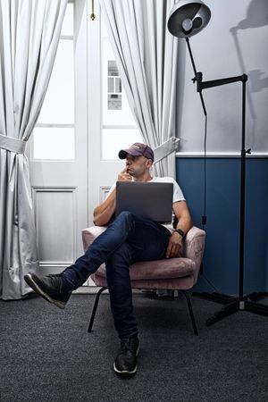 Man with cap sitting on armchair with a laptop