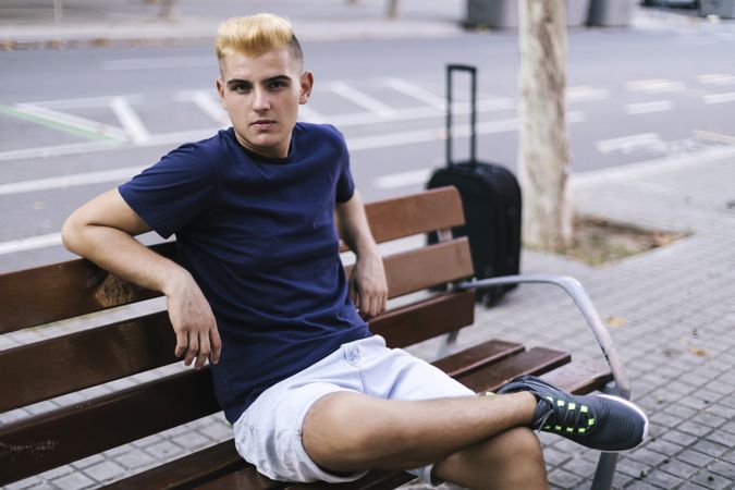 Portrait of man sitting on a bench with suitcase in the street