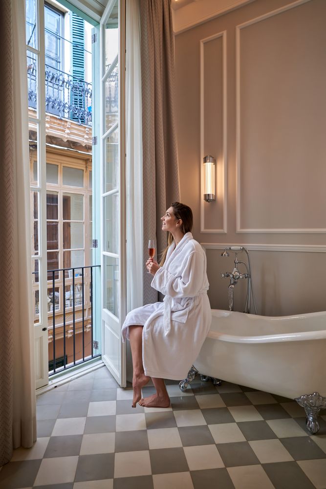 Woman in bathrobe on edge of bathtub champagne glass