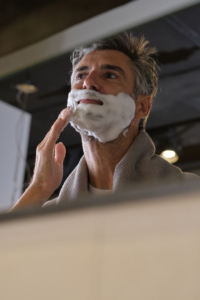 Happy male applying shaving foam in bathroom