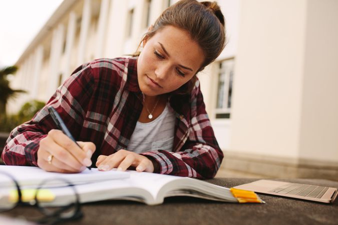 Female student sitting at college campus and making notes