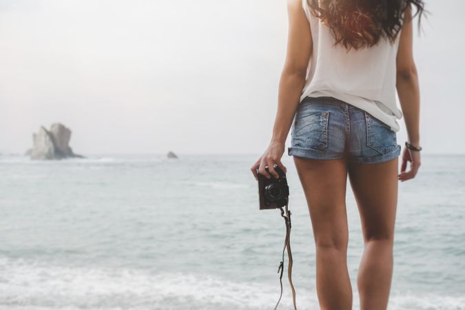 Woman with camera on shore near stones and water