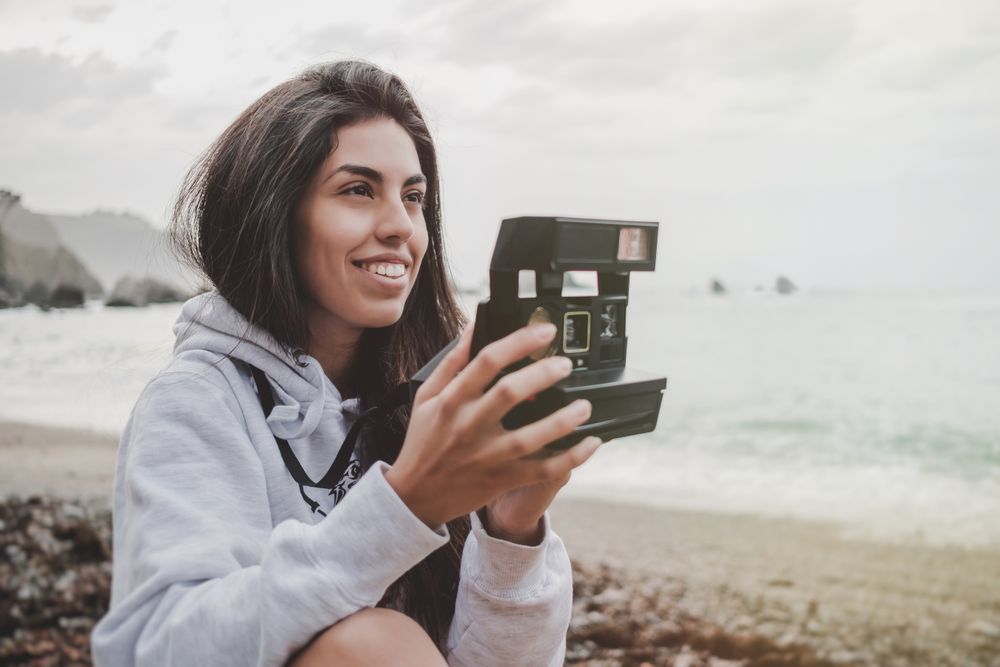 Woman with camera on shore near stones and water
