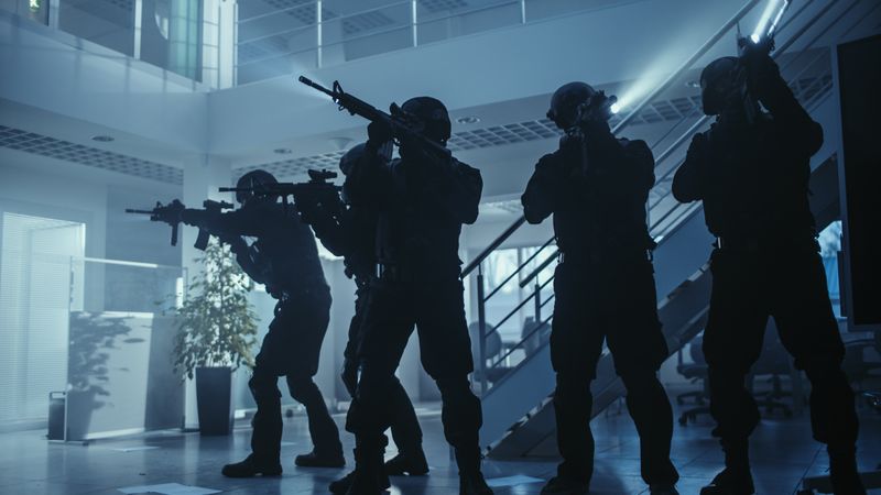 Masked Squad of Armed SWAT Police Officers Stand in Dark Seized Office Building with Desks and Computers.