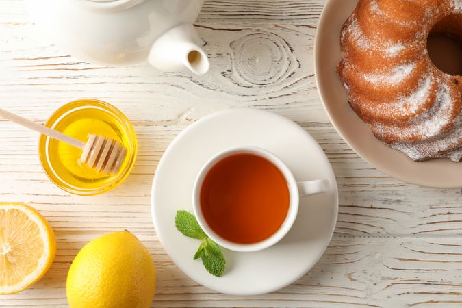 Cup of tea, lemon, mint, honey, dipper and pie on wooden background, top view