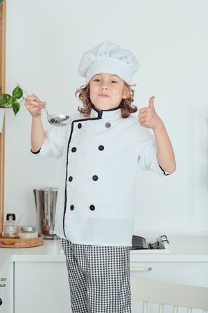 Cheerful little boy testing food from spoon in kitchen