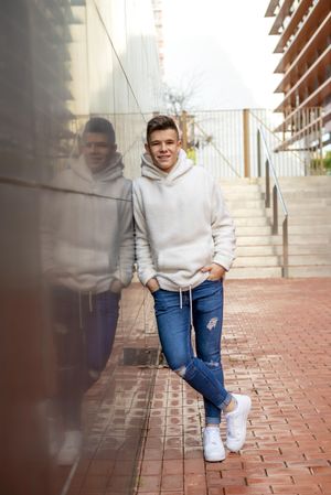 Portrait of young male with hands on pocket leaning on wall outside by staircase, vertical