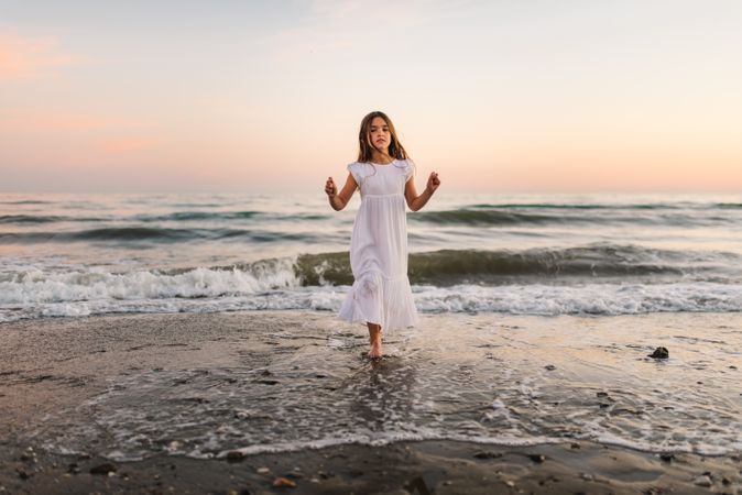Adorable girl walking and playing on seaside at sunset