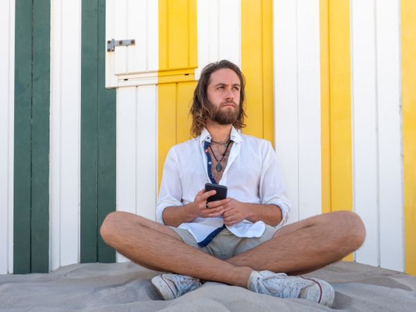 Cheerful guy using smartphone near striped wall