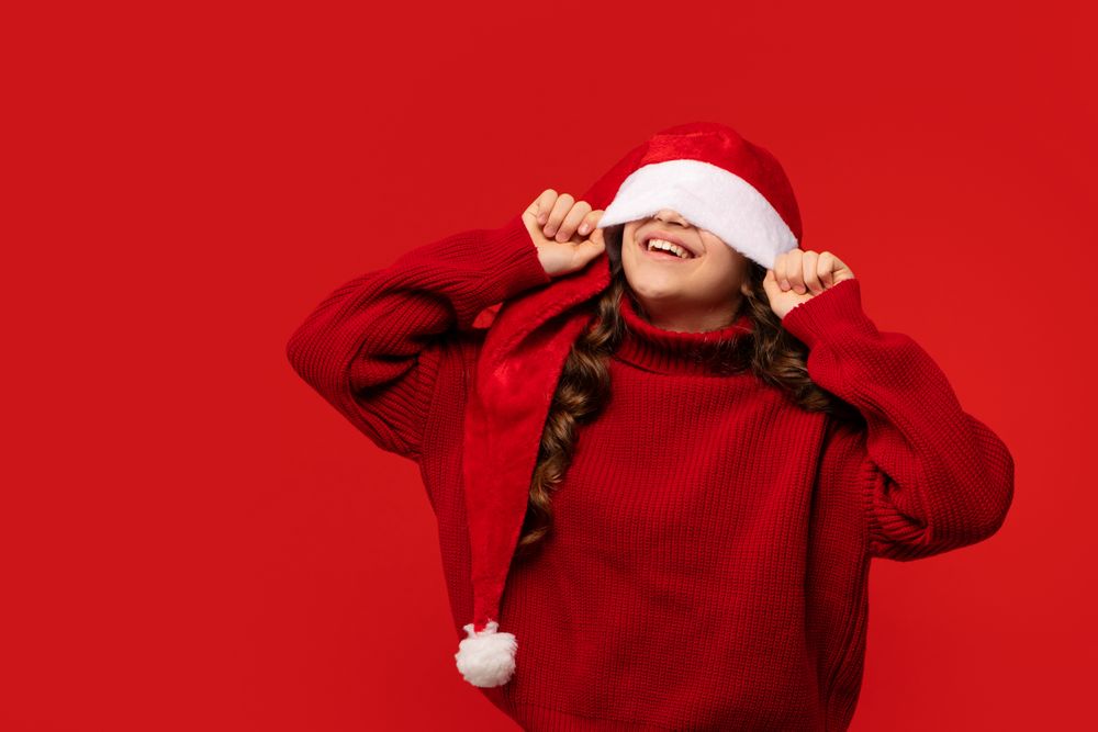 Girl playfully pulling Santa hat over eyes while smiling.