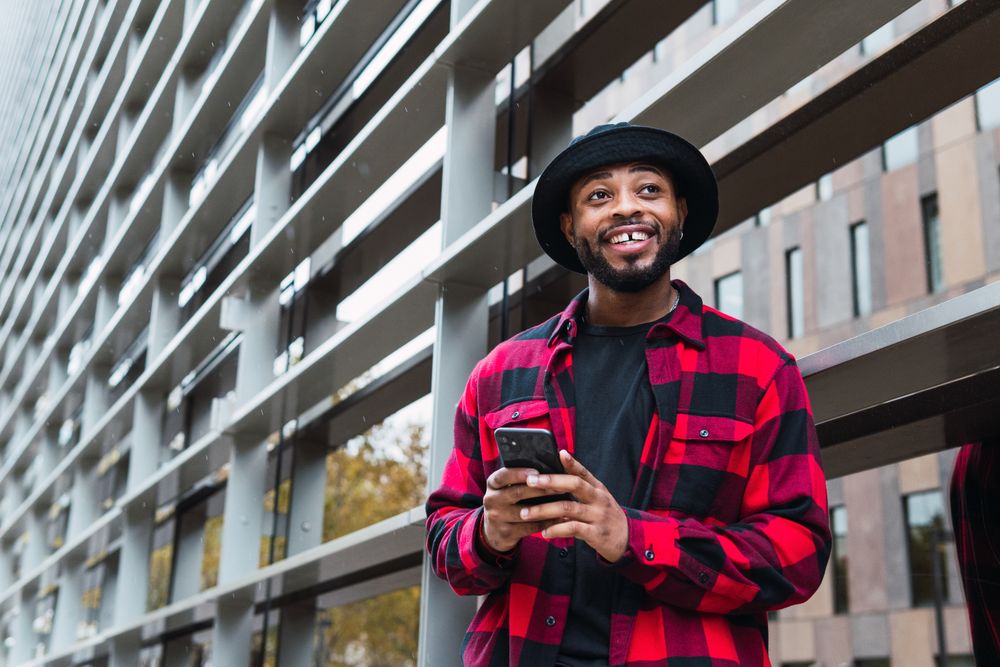 Cheerful Black male with smartphone in contemporary building