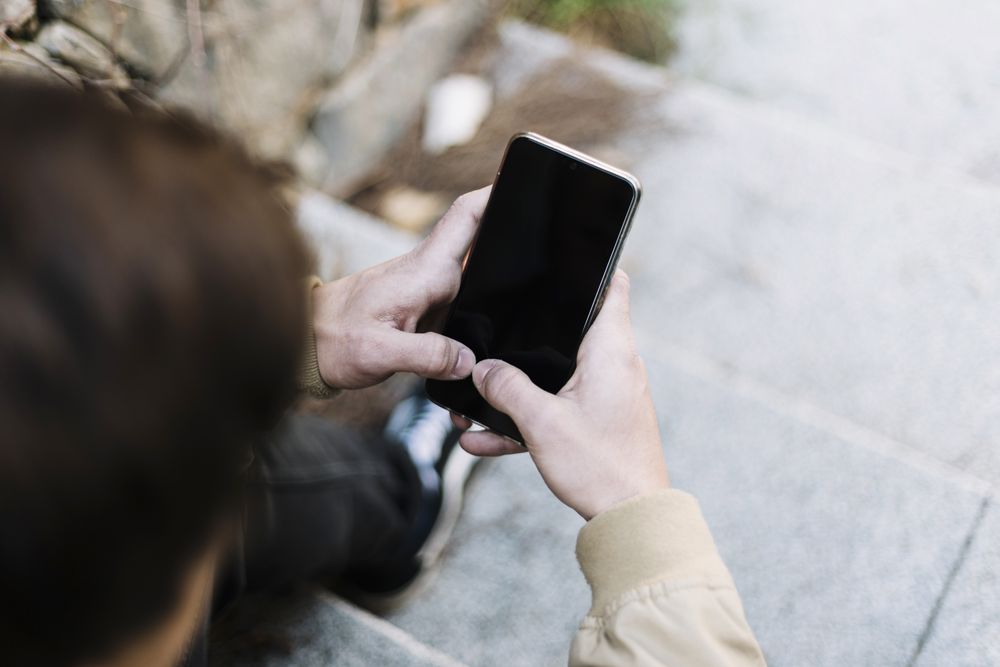 Rear view of young man using mobile phone while sitting outdoors