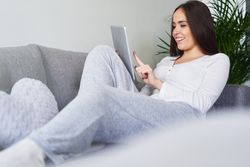 Smiling woman browsing on tablet and sitting on settee