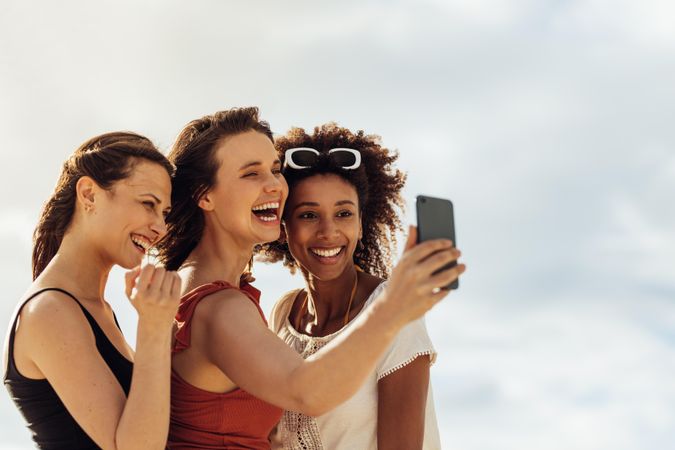 Happy woman taking selfie with friends using mobile phone
