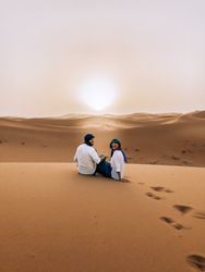 Man and woman sitting on sand dune in desert in Errachidia, Morocco