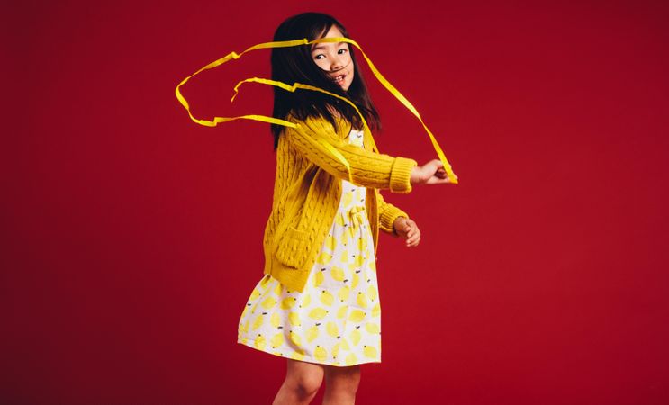 Little girl playing with a yellow satin ribbon standing against a red background