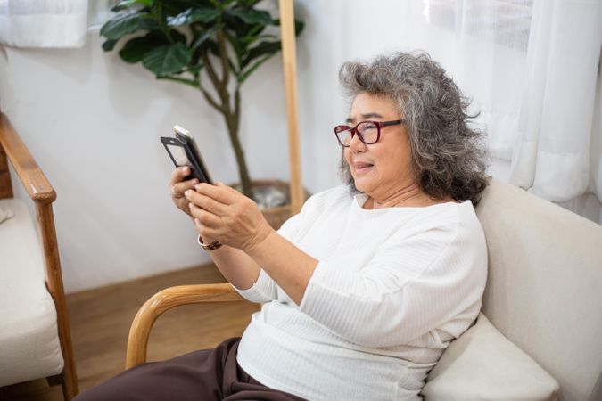Older woman smiling and sitting on couch using smartphone