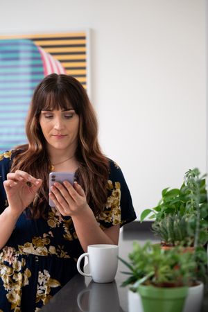 Female in floral print dress checking phone in a break room with coffee and plants