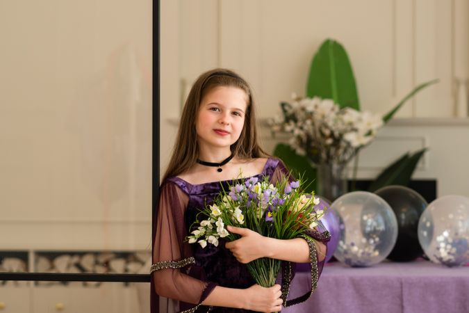 Girl holding flowers at birthday party with balloons.