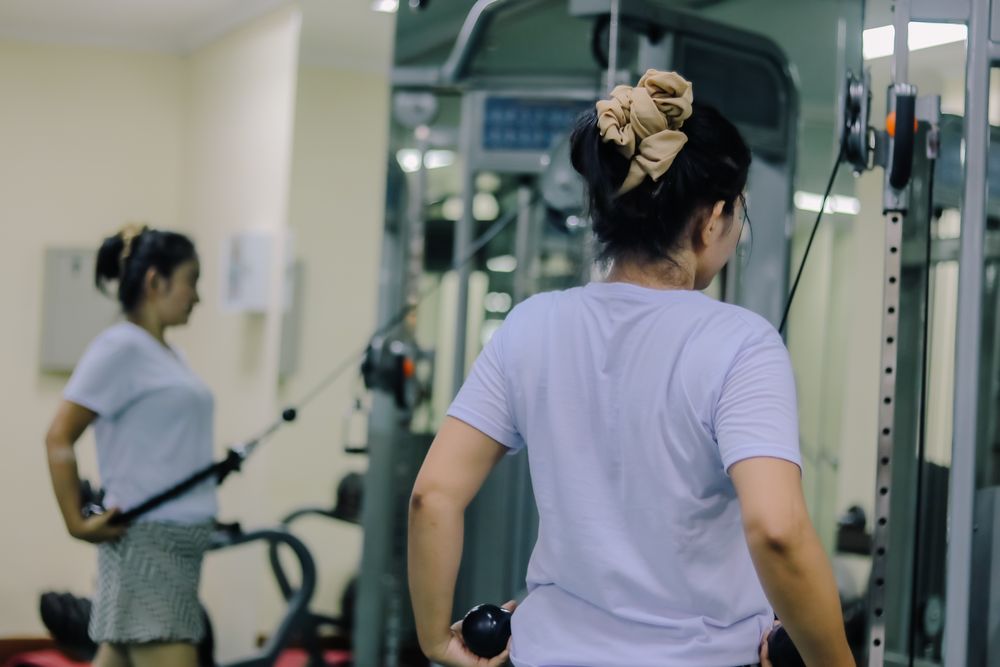 women doing physical activity in the gym operating a cable weight machine using both hands.