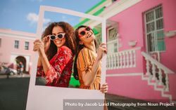 Beautiful female friends wearing sunglasses and holding a blank picture frame 48oLJ5